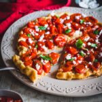 tarte tatin con pomodorini e feta su piatto bianco con fetta tagliata