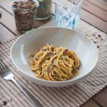 Pasta estiva con crema di zucchine e pomodori su tovaglietta con bicchiere e posate