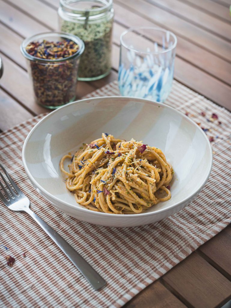 Pasta estiva con crema di zucchine e pomodori su tovaglietta con bicchiere e posate
