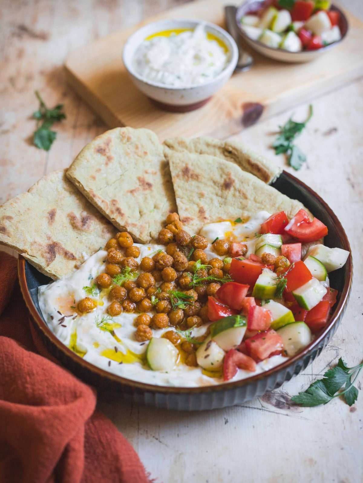 Piatto fondo con pane, ceci, tzatziki, verdure e ciotoline su tavolo