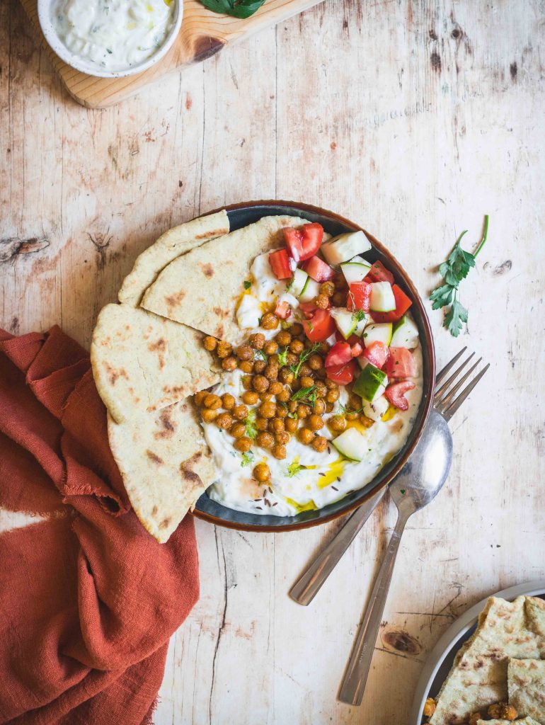 Piatto con pane, ceci, verdure e tzatziki con posate su tavolo