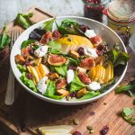 Piatto di insalata autunnale con fichi, pere e grano su tagliere di legno con ingredienti e posate