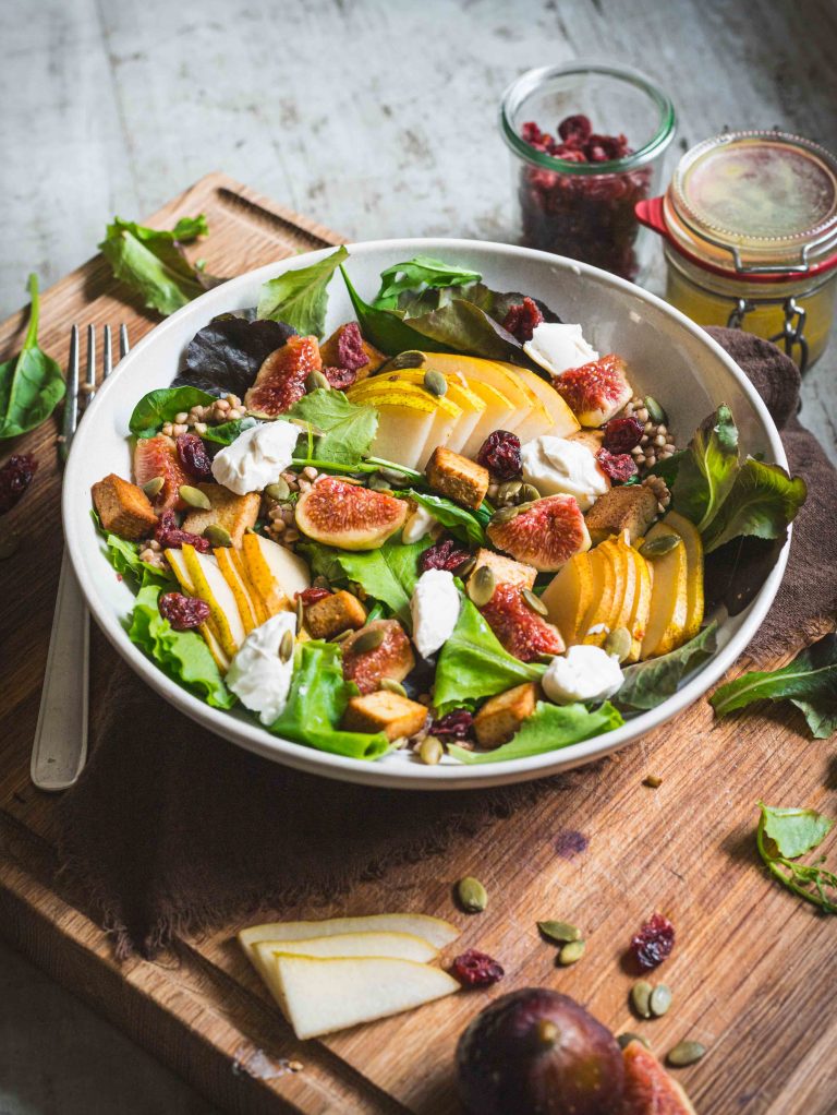 Piatto di insalata autunnale con fichi, pere e grano su tagliere di legno con ingredienti e posate