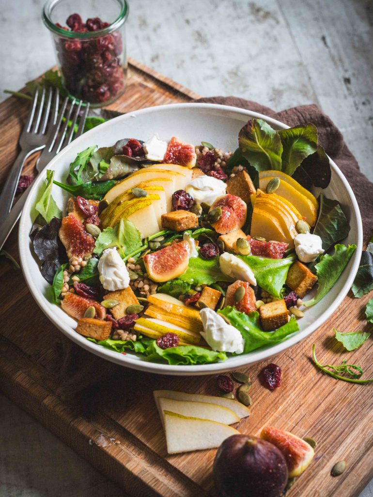 Ciotola di insalata autunnale con fichi, pere, grano su tagliere in legno