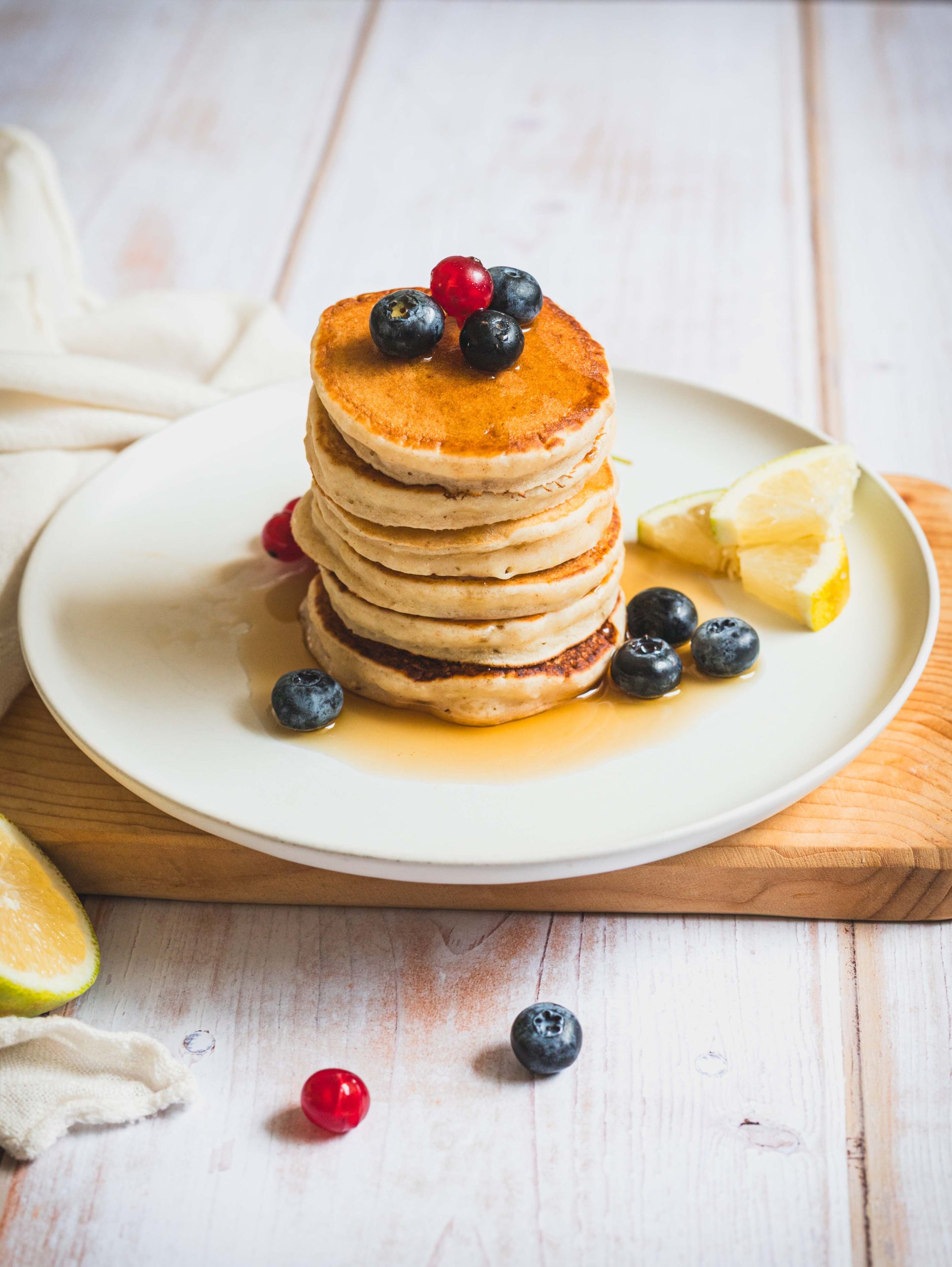 Torre di pancakes con yogurt vegetale e limone su piatto e tagliere