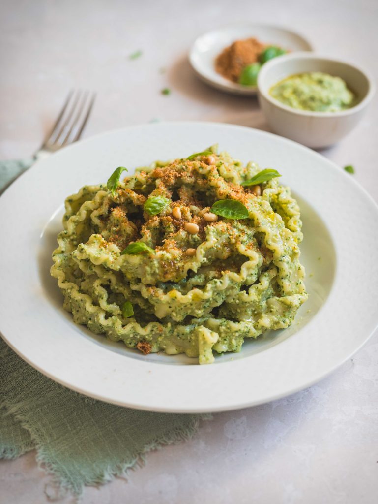 Piatto di pasta al pesto crudo con forchetta e due ciotoline di condimenti