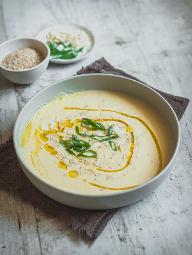 Piatto con vellutata di cavolfiore bianco su tovagliolo marrone con due ciotoline di ingredienti