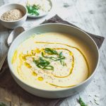 Piatto di vellutata di cavolfiore bianco con ciotoline e cucchiaio su tavolo in legno