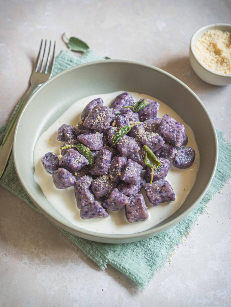 Piatto con gnocchi di cavolo viola, salvia e panna vegetale su canovaccio turchese e forchetta