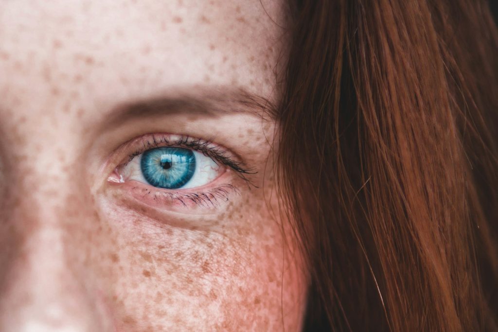 Occhio azzurro di ragazza dai capelli rossi in primo piano