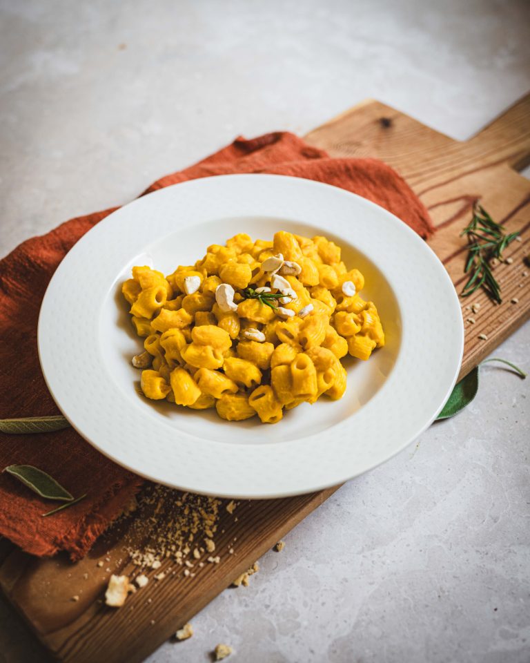 Pasta con sugo vegetale di zucca e cannellini in piatto bianco su tagliere