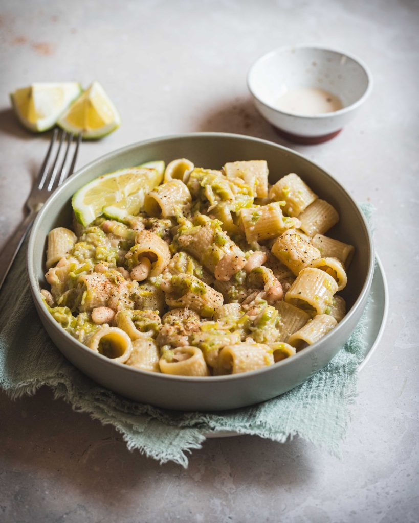 Pasta con porri, limone e cannellini in piatto fondo con canovaccio azzurro e forchetta
