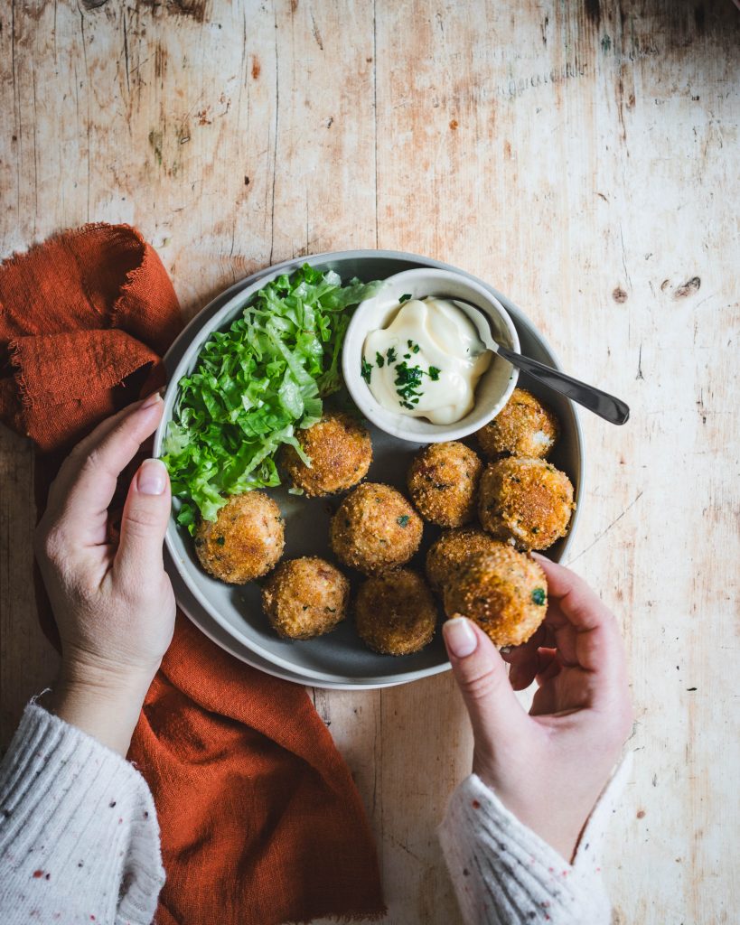 Piatto di polpette vegane di miglio, cavolfiore e cannellini in piatto con salsina e canovaccio rosso su tavolo in legno