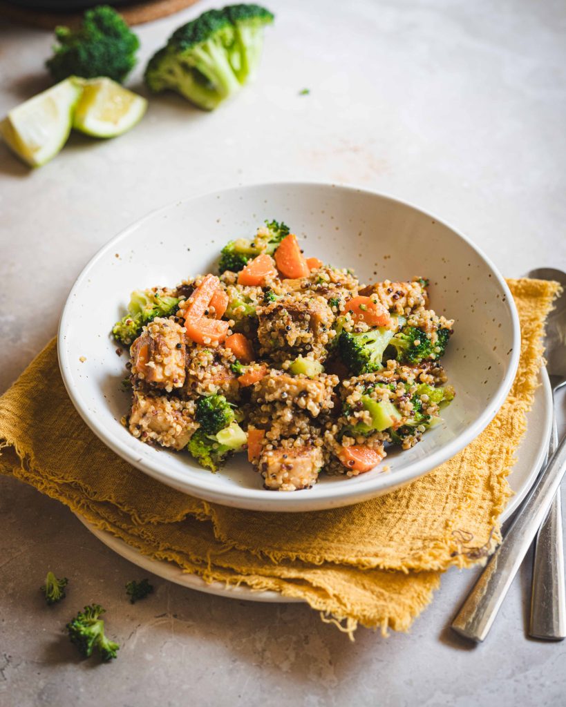 Tempeh stir fry in piatto fondo bianco con canovaccio giallo e posate